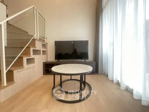 Modern living room with stylish staircase and large TV, featuring natural light and elegant decor.