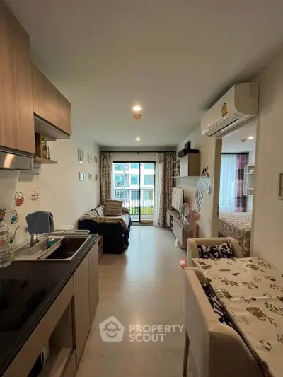Modern apartment interior with open kitchen and cozy living area leading to a balcony with a view.