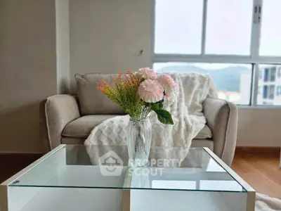Cozy living room with elegant sofa and glass coffee table, featuring a vase of flowers and a scenic window view.