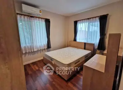 Cozy bedroom with wooden flooring and large windows in a modern apartment.