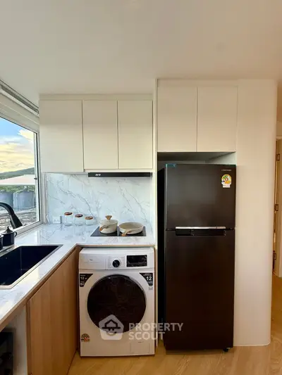 Modern kitchen with sleek appliances and marble backsplash, featuring a washing machine and fridge.