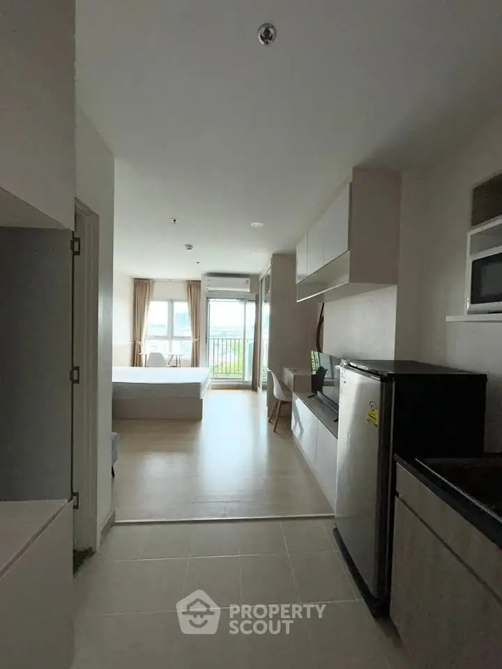 Modern studio apartment with open layout, featuring a compact kitchen and bright living area leading to a balcony.
