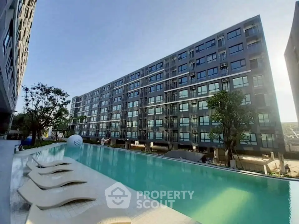 Modern apartment complex with a luxurious pool and sun loungers, perfect for relaxation.