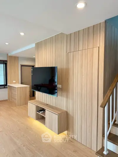 Modern living room with wooden paneling and mounted TV, featuring sleek design and natural lighting.