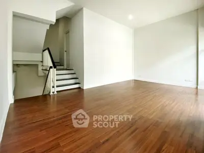 Spacious empty room with wooden flooring and staircase, perfect for customization.
