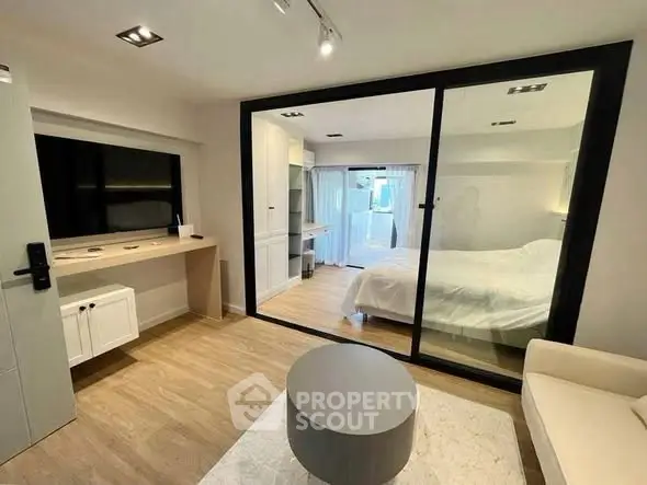 Modern apartment with glass-walled bedroom and stylish living area, featuring sleek furniture and natural light.