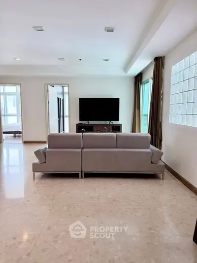 Spacious modern living room with sleek sofa and large TV, abundant natural light from windows.