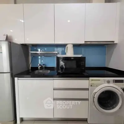 Modern kitchen with sleek cabinets, microwave, and washing machine in compact layout.
