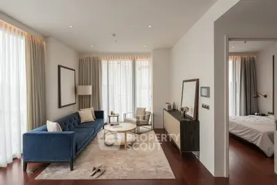 Elegant modern living room with blue sofa, stylish decor, and natural light, adjacent to a cozy bedroom.