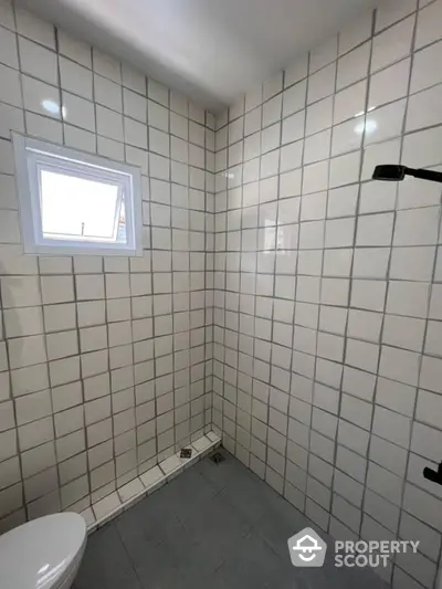 Pristine white-tiled bathroom with modern fixtures and a small frosted window allowing for natural light and ventilation.