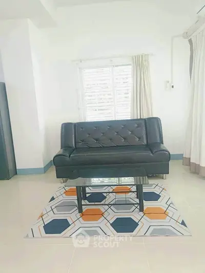 Modern living room with stylish black sofa and geometric rug, featuring a sleek glass coffee table.