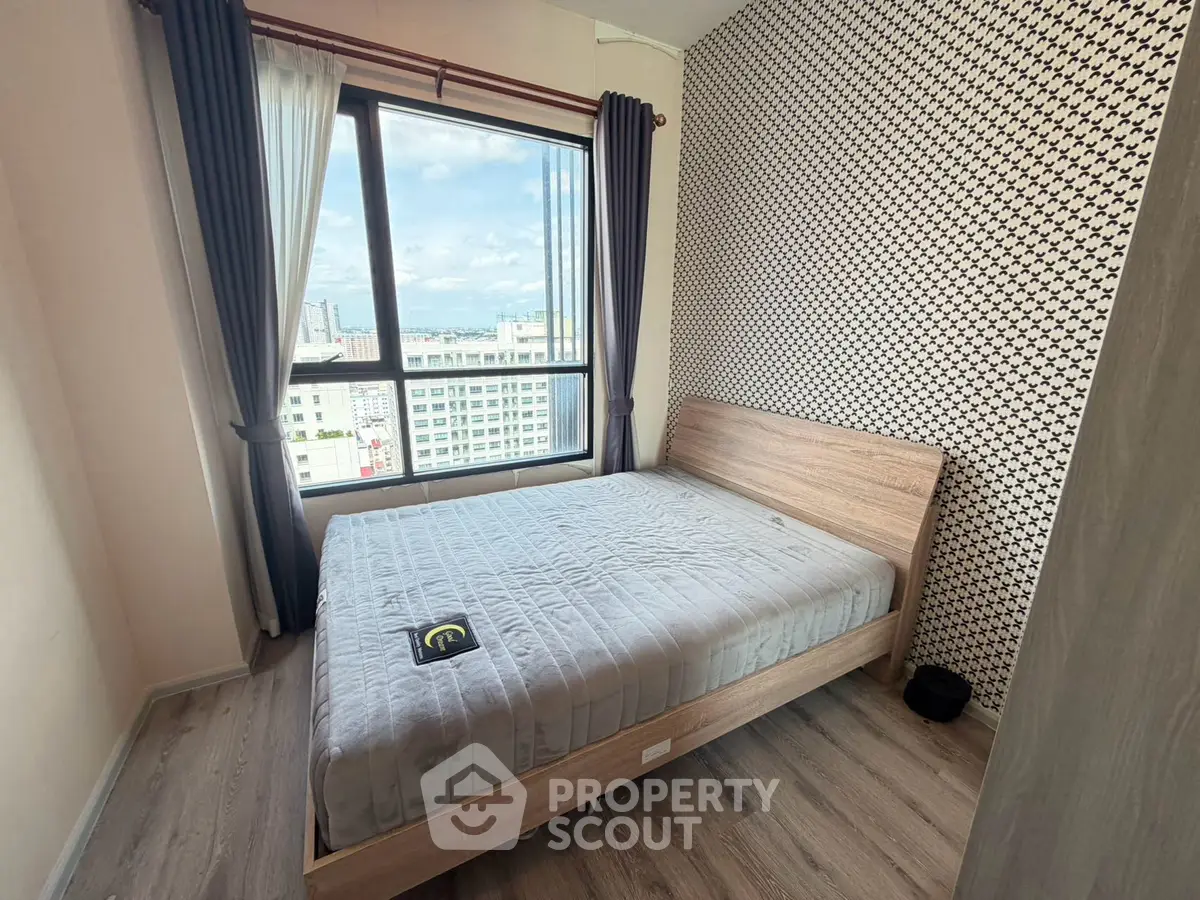Modern bedroom with large window offering city views and stylish wallpaper accent wall.