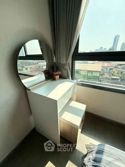 Bright bedroom corner with vanity table and city view through large window.