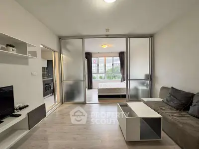 Modern open-plan living room with sliding doors to bedroom, featuring sleek furniture and ample natural light.