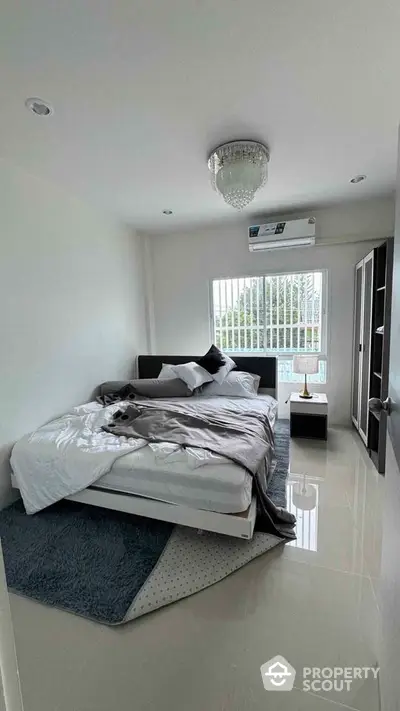 Modern bedroom with elegant chandelier and large window offering natural light.