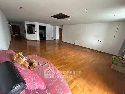 Spacious empty living room with wooden flooring and red sofa, ideal for renovation.