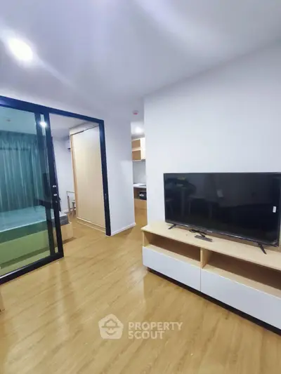 Modern apartment interior with open living room and bedroom, featuring sleek TV stand and wooden flooring.