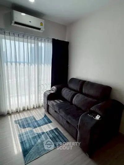 Cozy living room with plush sofa and air conditioning, featuring large window with sheer curtains.