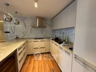 Modern kitchen with sleek cabinetry and marble backsplash, featuring a gas stove and stylish lighting.