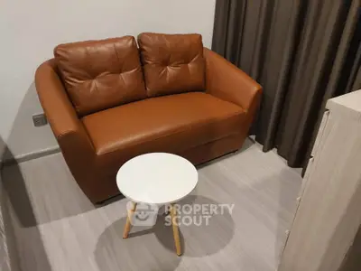 Cozy living room with brown leather loveseat and small round table, perfect for relaxation.