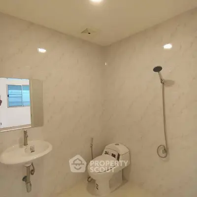 Modern bathroom with sleek fixtures and marble walls, featuring a shower and toilet.