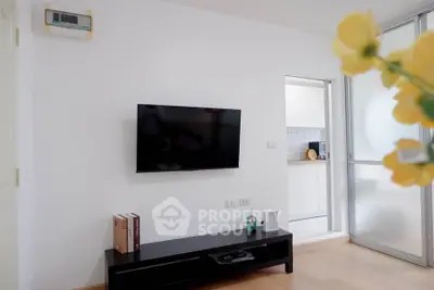 Modern living room with wall-mounted TV and sleek furniture, open view to a stylish kitchen.