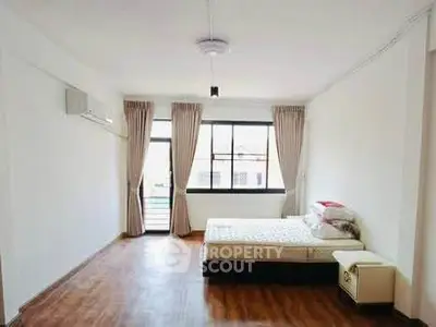 Spacious bedroom with wooden flooring and large window for natural light.
