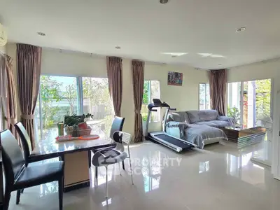 Spacious living room with treadmill and dining area, large windows, and modern decor.