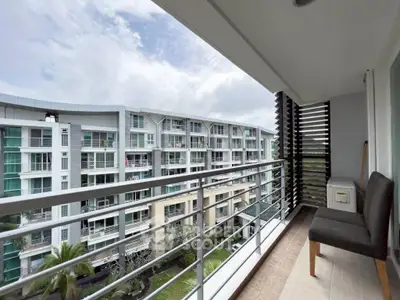 Spacious balcony with seating offering a view of modern residential buildings and lush greenery.