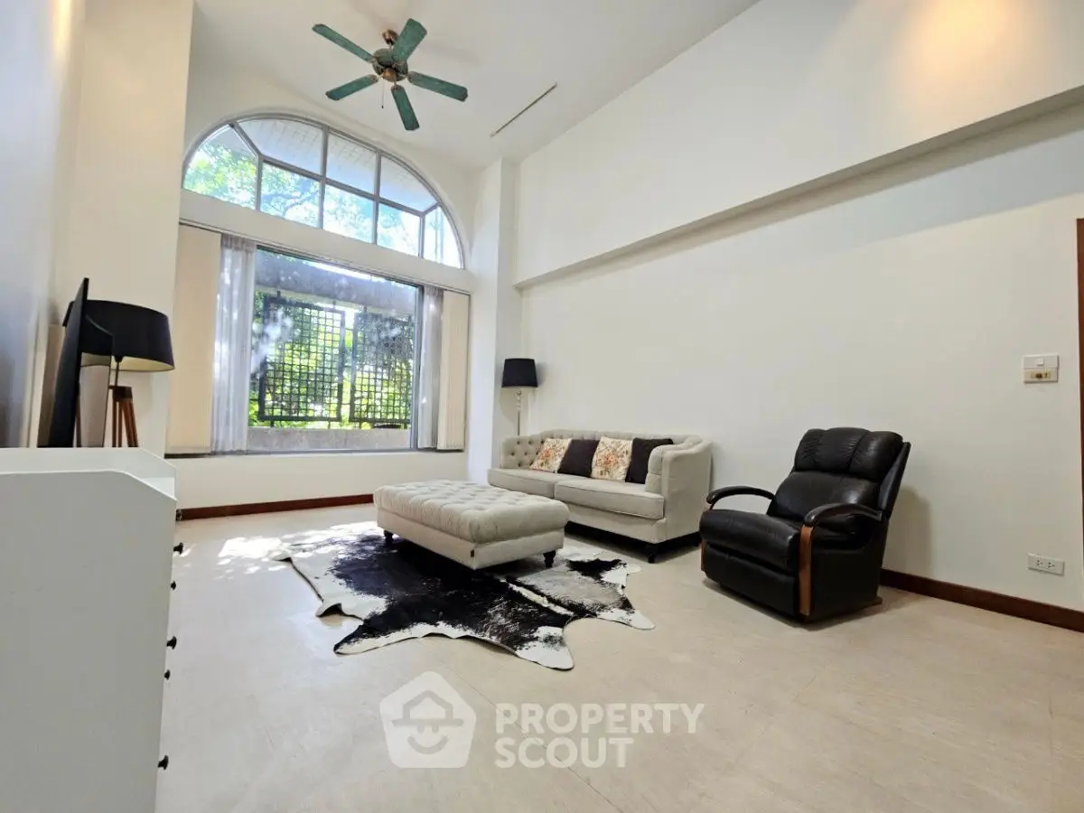 Spacious living room with high ceiling, modern furniture, and large window for natural light.