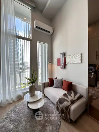 Modern living room with high ceilings, large windows, and stylish decor in a city apartment.