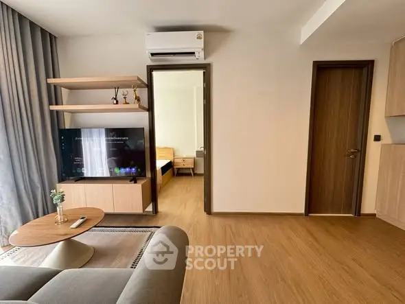 Modern living room with wooden flooring and stylish furniture leading to a cozy bedroom.