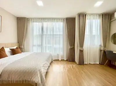 Spacious bedroom with elegant curtains and wooden flooring, featuring a cozy bed and modern decor.
