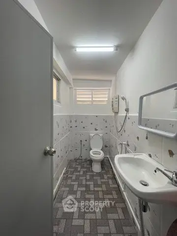 Compact bathroom with modern fixtures and tiled flooring, featuring a toilet and sink under bright lighting.