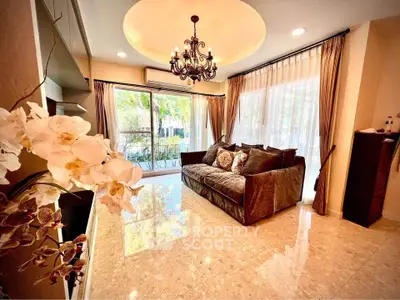 Luxurious living room with elegant chandelier and large windows offering garden views.