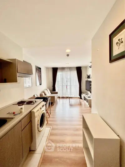 Modern open-plan living room with kitchen, featuring wooden flooring and natural light.