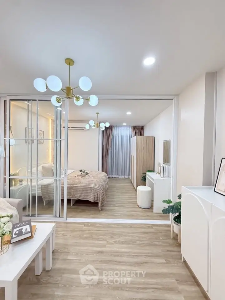 Modern open-plan living room with stylish decor and cozy bedroom view, featuring elegant lighting and wooden flooring.