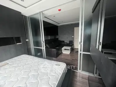 Modern bedroom with sliding glass doors leading to a stylish living area, featuring sleek dark furnishings.