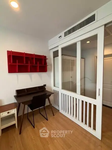 Modern study room with stylish desk and red wall shelf, featuring sliding glass doors and wooden flooring.