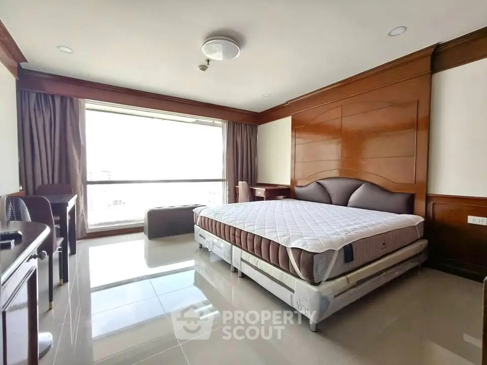 Spacious bedroom with large window and elegant wooden paneling, offering abundant natural light and modern comfort.
