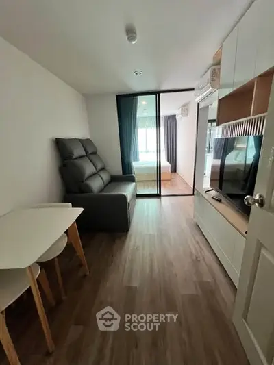 Modern apartment interior with open living room and bedroom view, featuring sleek furniture and wooden flooring.