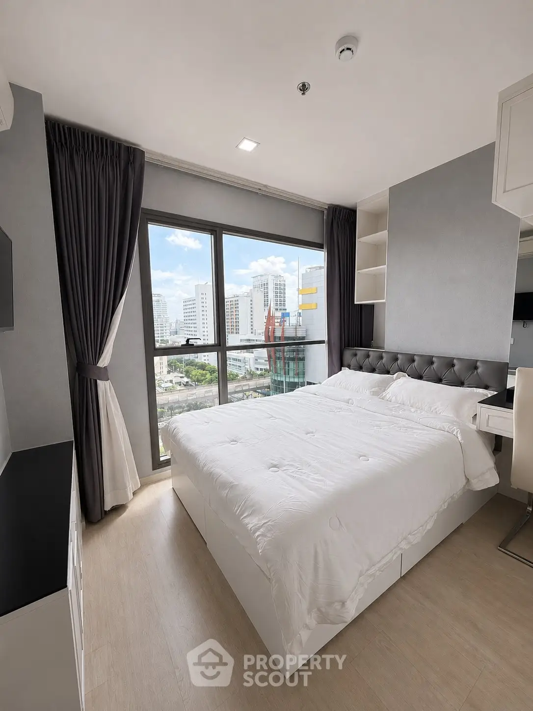 Modern bedroom with city view, featuring elegant decor and large window for natural light.