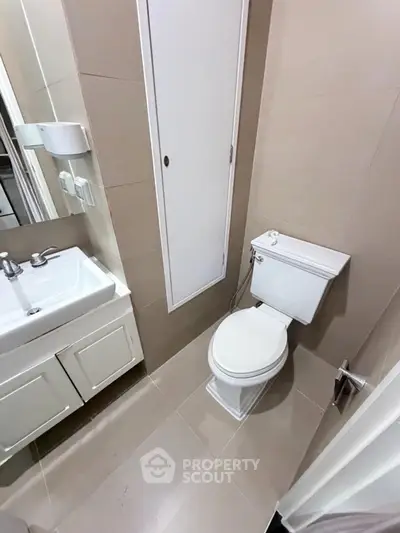 Compact bathroom with modern fixtures and neutral tiles, featuring a sleek sink and toilet.