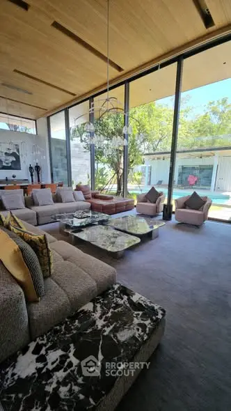 Luxurious living room with floor-to-ceiling windows and garden view, featuring elegant furniture and modern decor.
