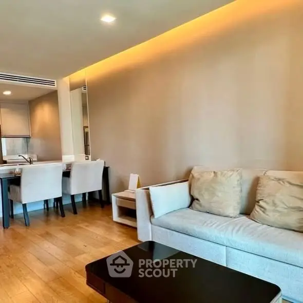Modern living room with cozy sofa and dining area, featuring warm lighting and wooden flooring.