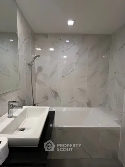 Modern bathroom with sleek marble tiles and a stylish sink and bathtub.