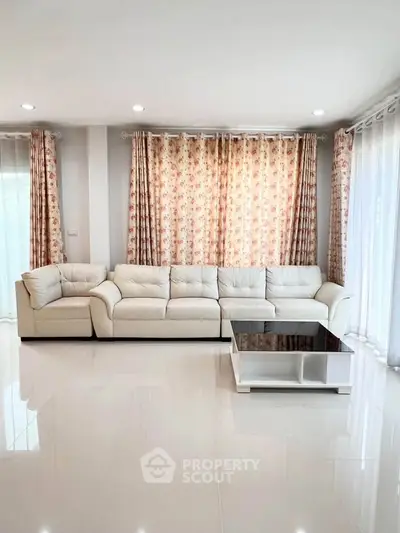 Spacious living room with elegant white sofa and floral curtains, perfect for relaxation and entertainment.