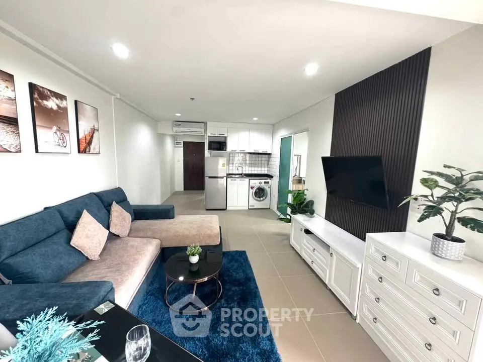 Modern living room with stylish decor, blue sofa, wall-mounted TV, and open kitchen layout.