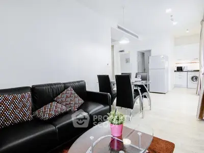 Modern living room with sleek black sofa and dining area in open layout apartment.