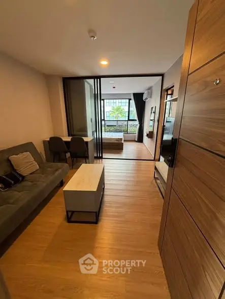 Modern open-plan living room with wooden flooring and stylish furniture, featuring a view of a cozy bedroom.